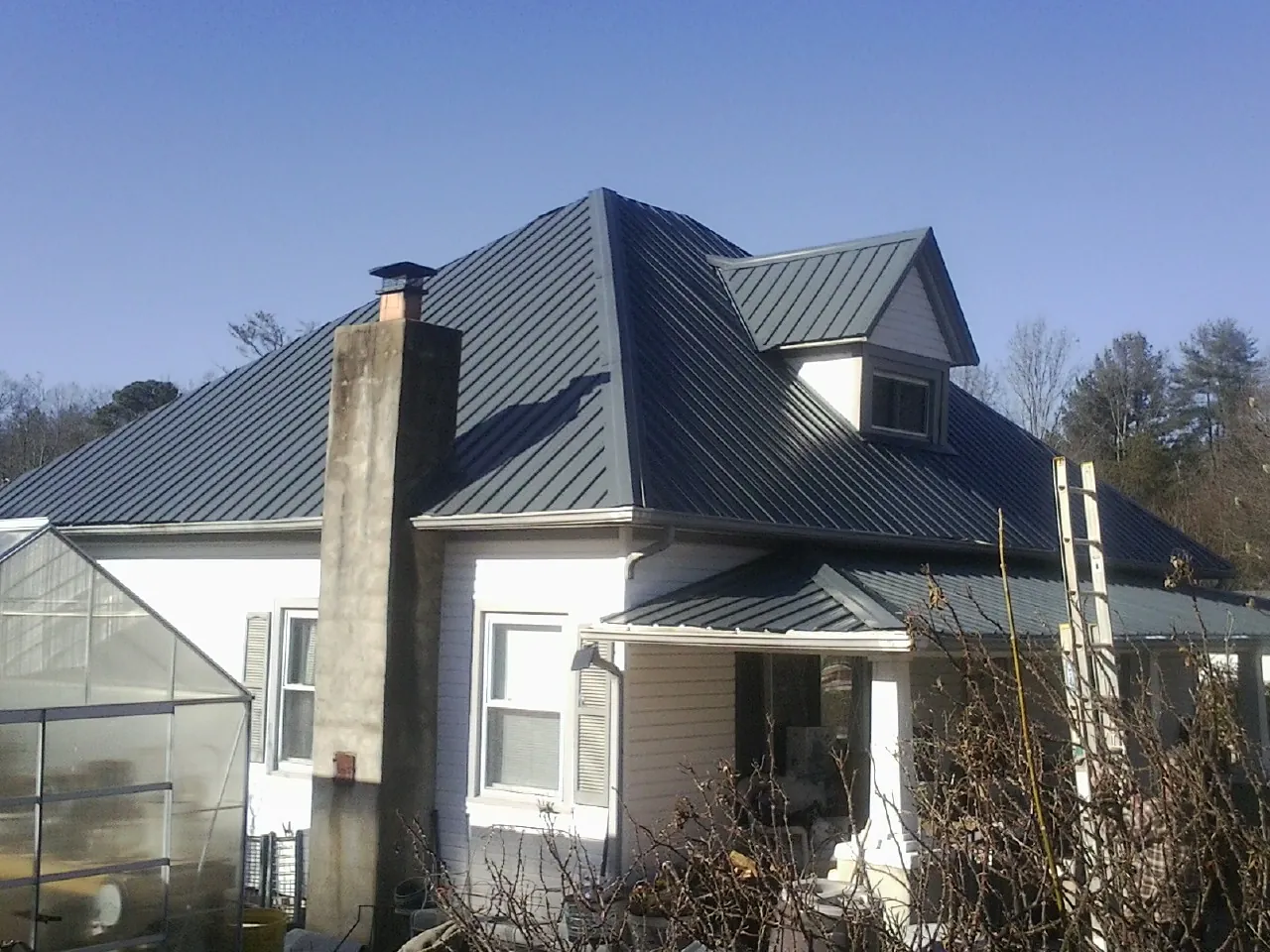 Dark blue standing seam metal roof on a white farmhouse with dormer — Slate & Tile Roof Repair by Roofing Brothers in Sequatchie