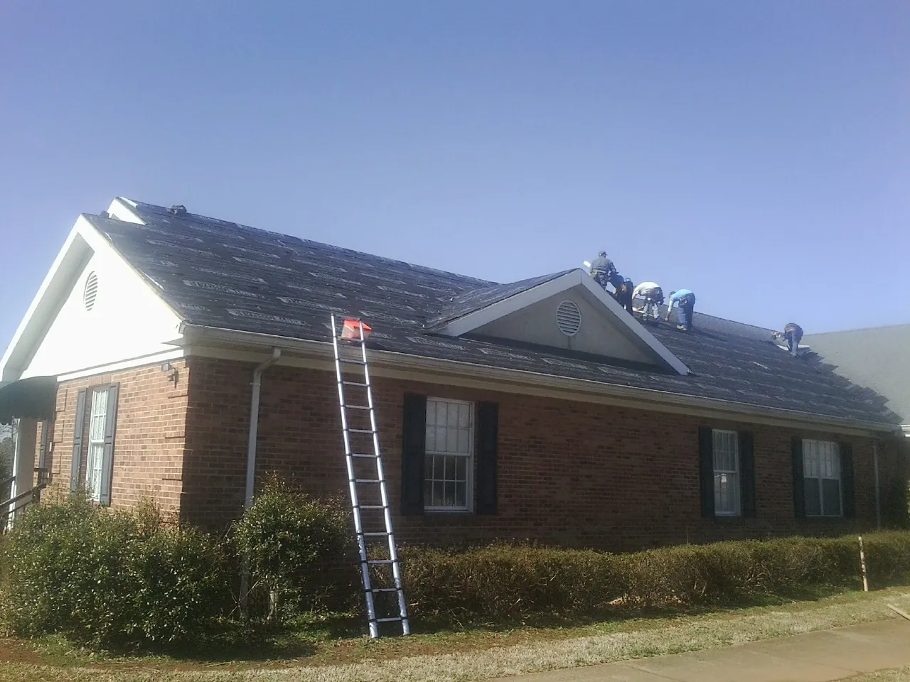 Crew tearing shingles off a brick ranch roof with a ladder set — Metal Roof Repair work by our crew in Sequatchie