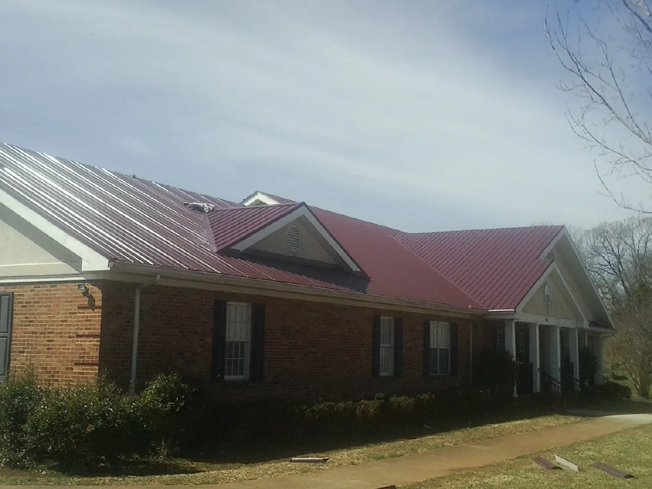 Red metal roof with gabled entries on a long brick building, from a Hail Damage Roof Repair job in Sequatchie
