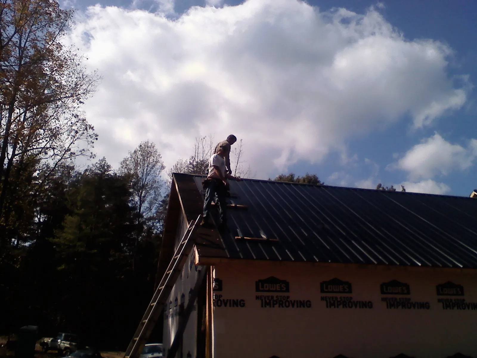 Roofer fastening dark metal panels high against a cloudy sky, from a Roof Inspection job in Sequatchie