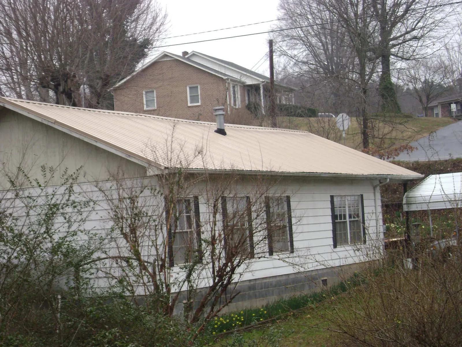 Tan metal roof on a white sided house set into a hillside — Commercial Roofing by Roofing Brothers in Sequatchie
